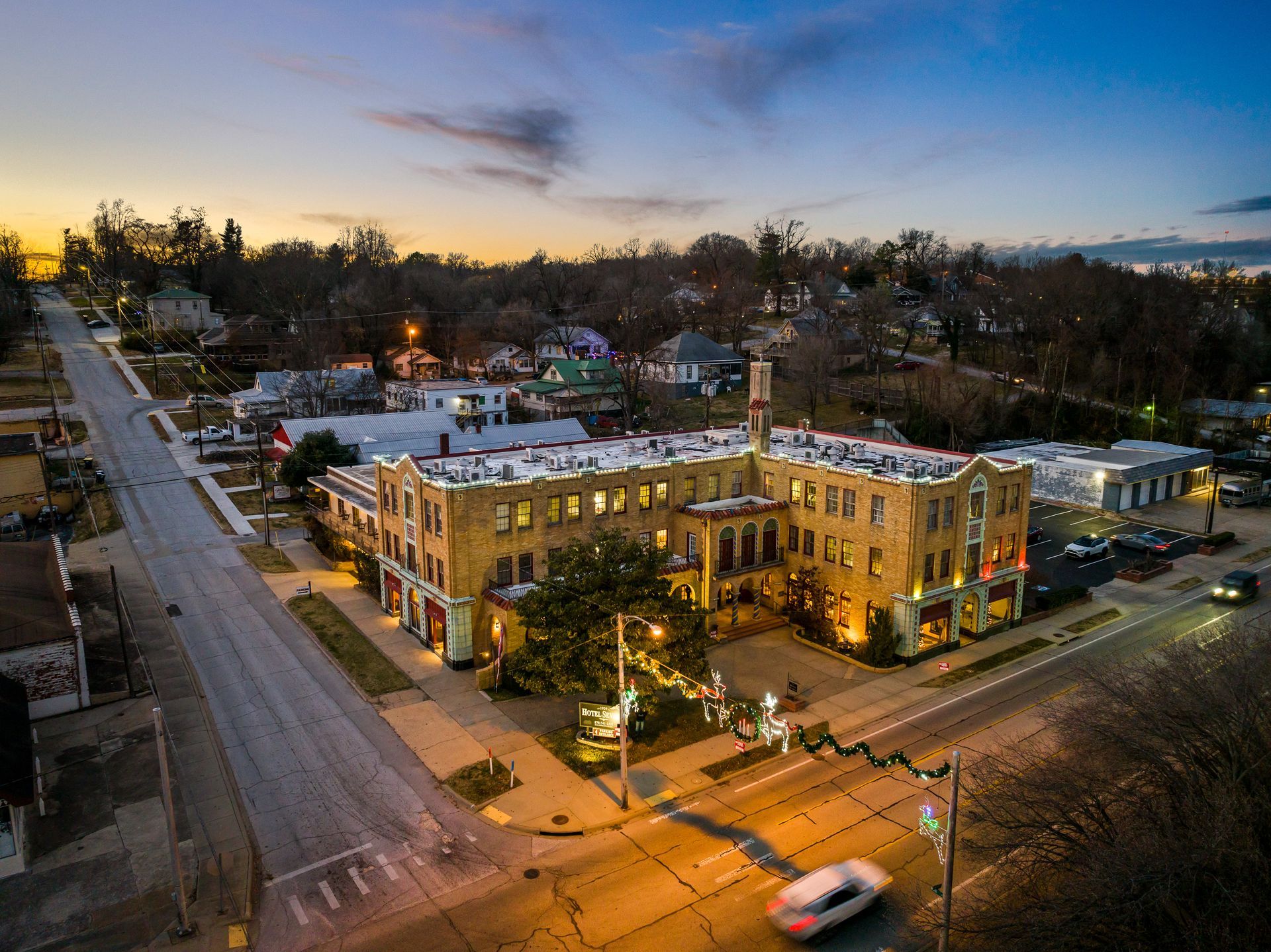 Aerial view of a brick building at dusk with surrounding neighborhood. Street and trees visible.