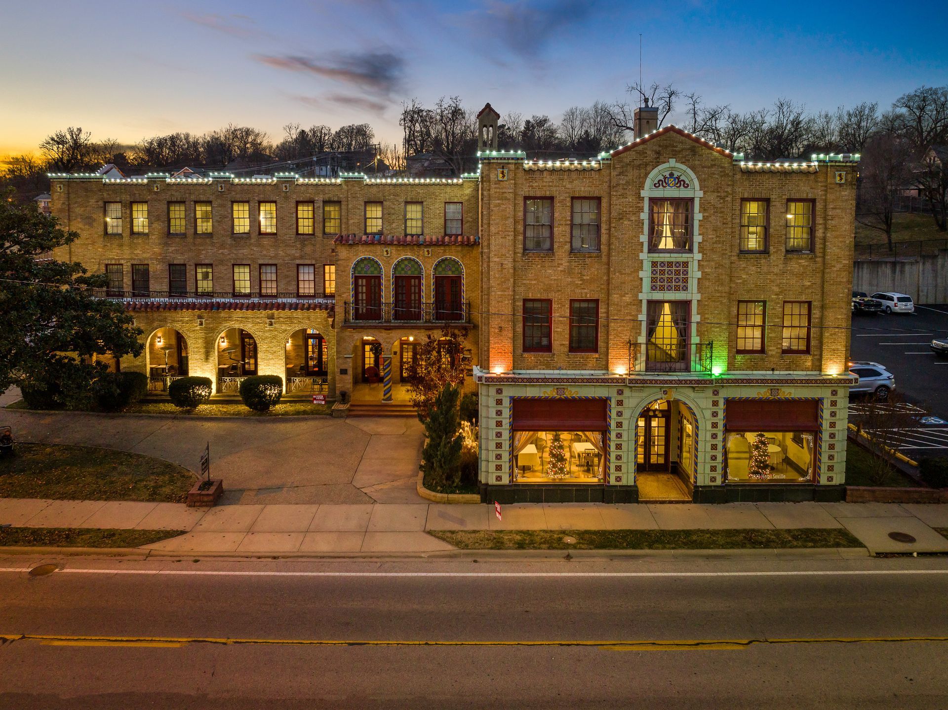 Historic building with Christmas lights, dusk setting. Beige brick facade with storefronts, overlooking a street.