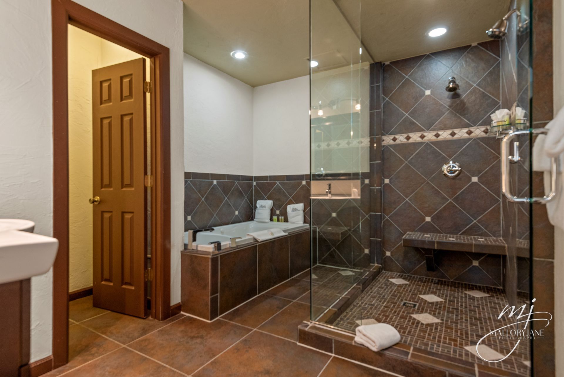 Bathroom with large glass shower, brown tile, and a bathtub.