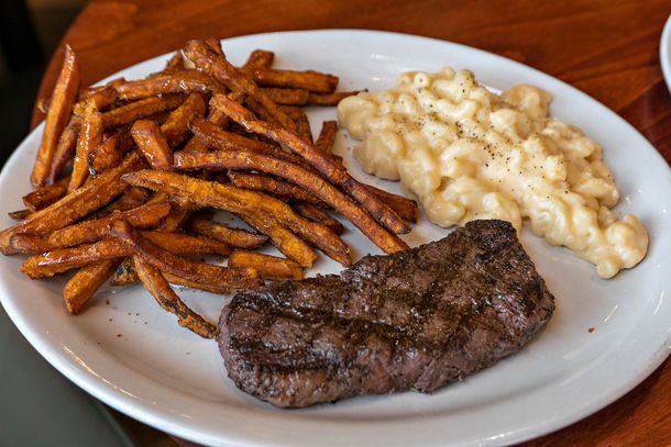 Steak, sweet potato fries, and mac & cheese on a white plate.