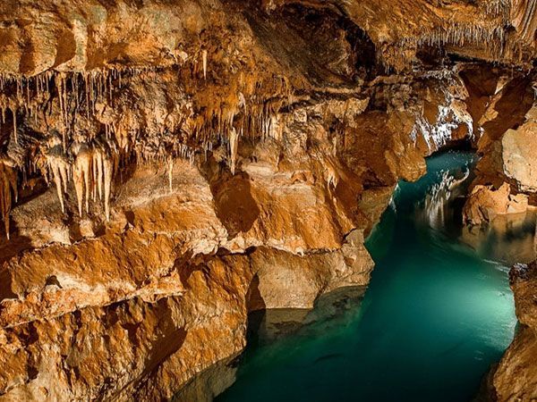 Cave with turquoise water, brown rock walls, stalactites hanging from the ceiling.