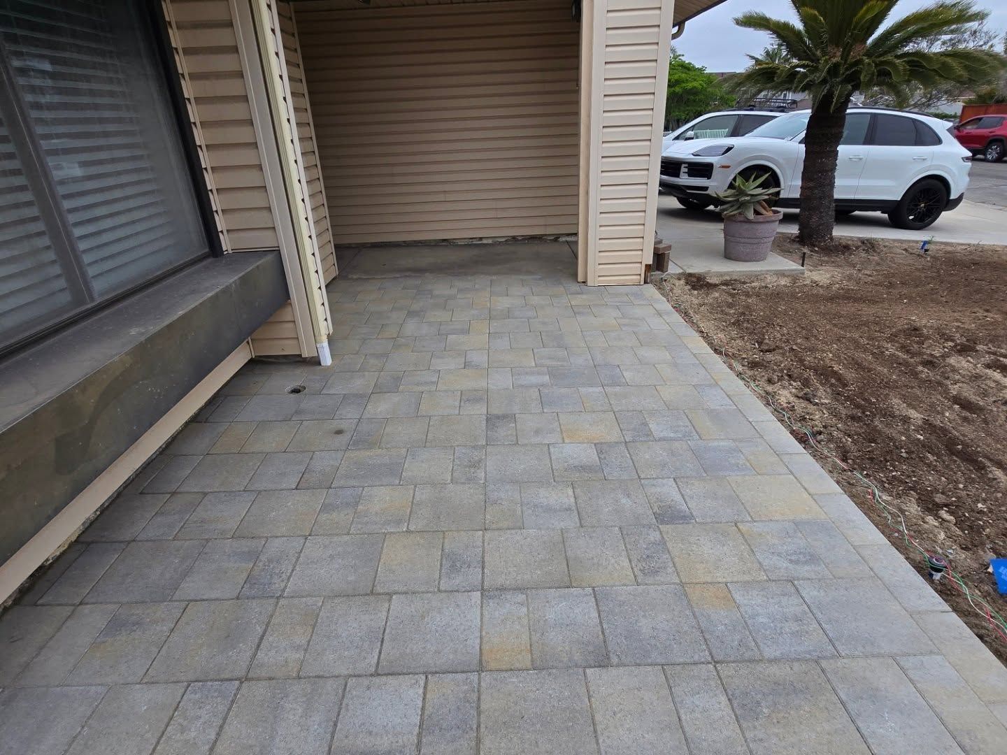 Stone pavers on a patio with building, cars, and palm tree in the background.