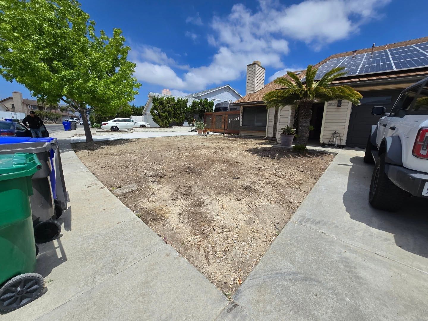Front yard with dry grass, sidewalk, and a house with solar panels on a sunny day.