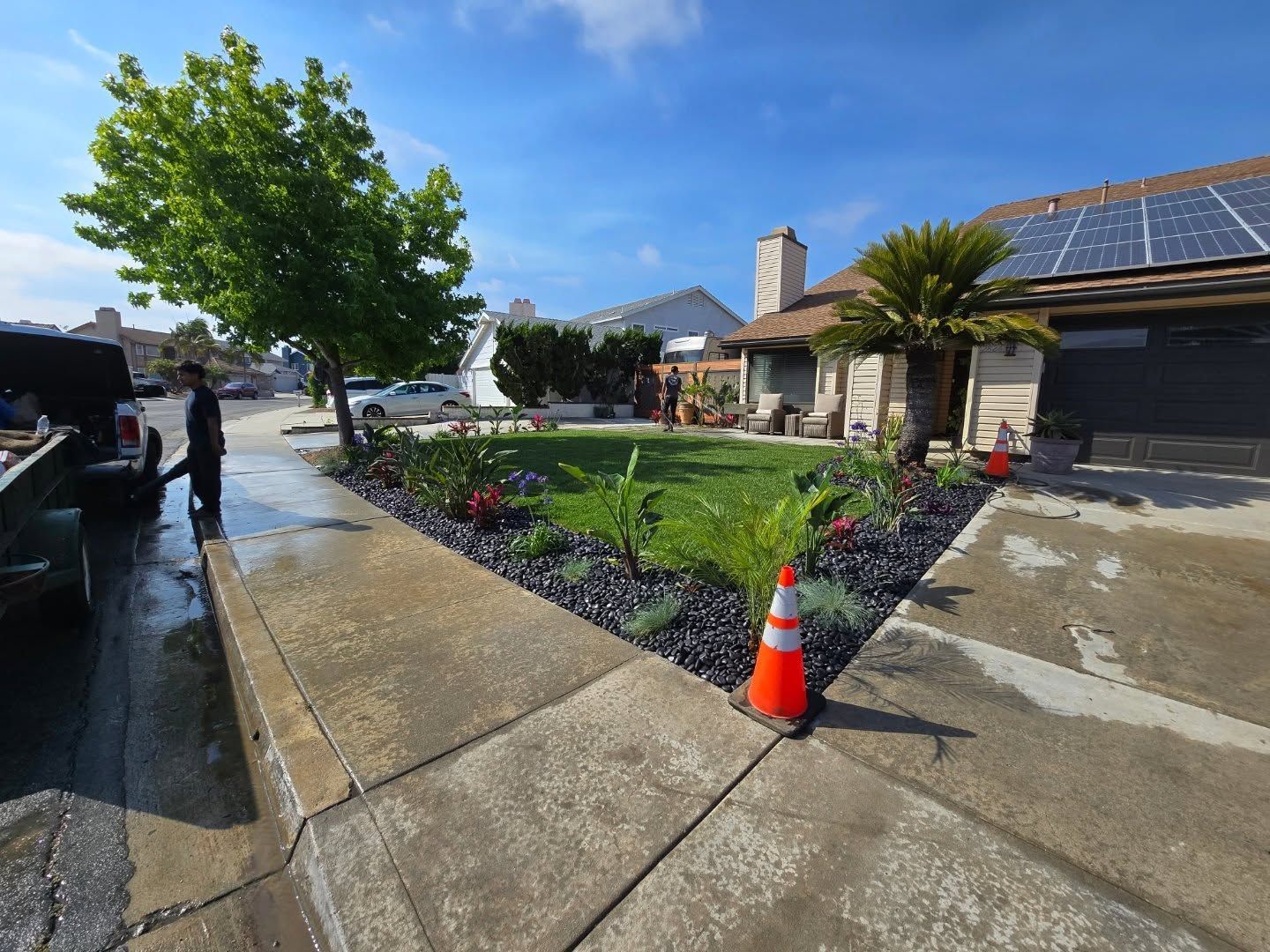 Landscaped front yard with black rock border, plants, grass, and a person blowing leaves.
