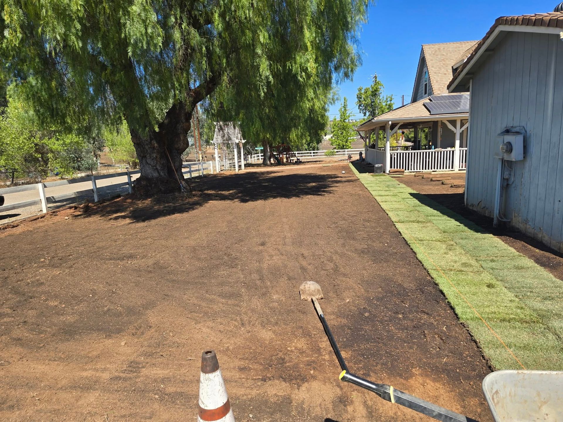 Yard being prepared for new grass, with installed sod alongside a building. Brown soil, green grass.