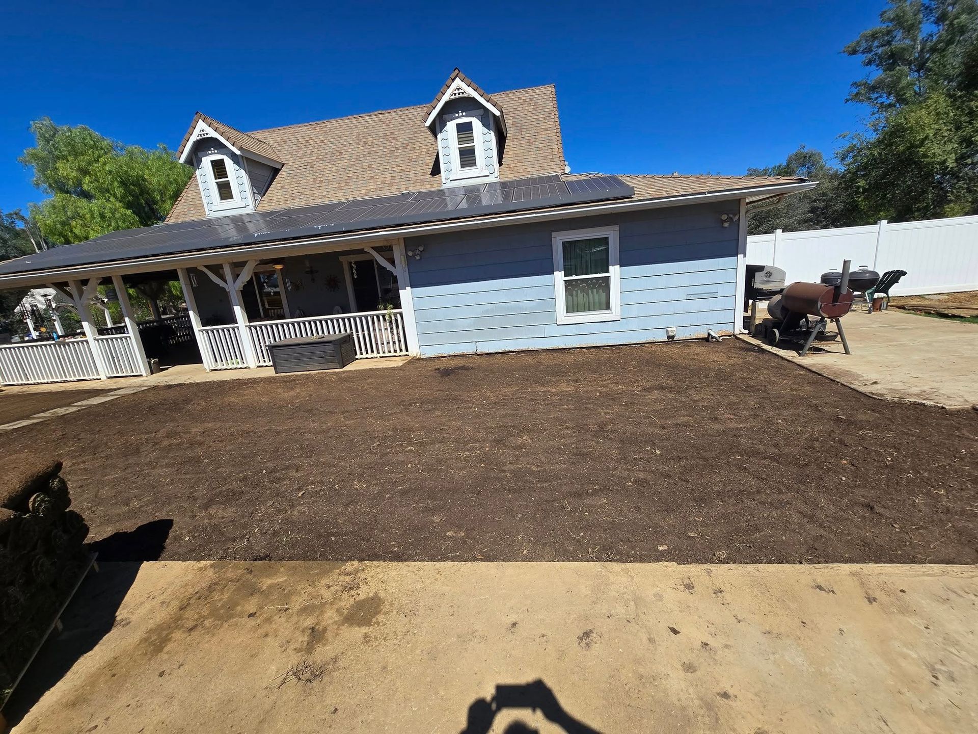 Blue house with brown roof, porch, and yard covered in fresh mulch. Clear blue sky.