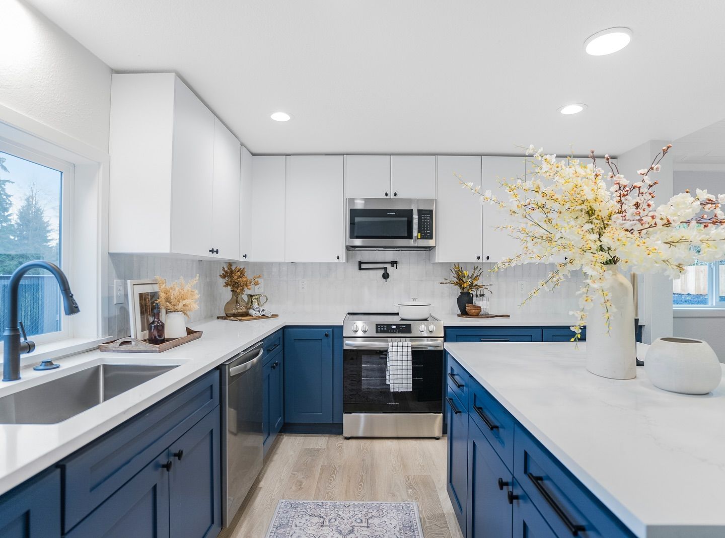 A kitchen with blue cabinets , white counter tops , stainless steel appliances and a sink.