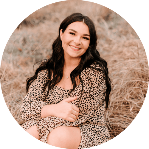 A woman in a leopard print dress is sitting in the grass and smiling.