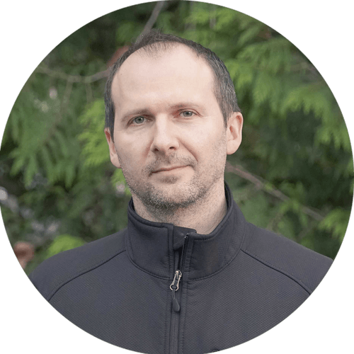 A man in a black jacket is standing in a circle with trees in the background.