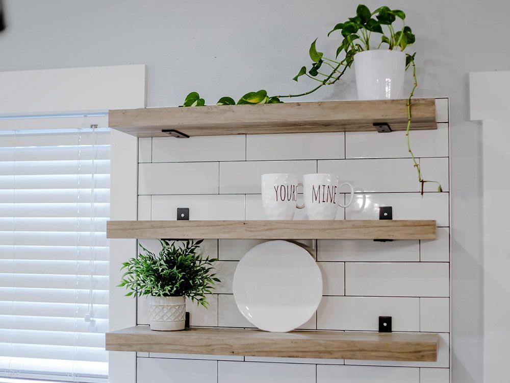 A kitchen with three wooden shelves filled with plates and potted plants.