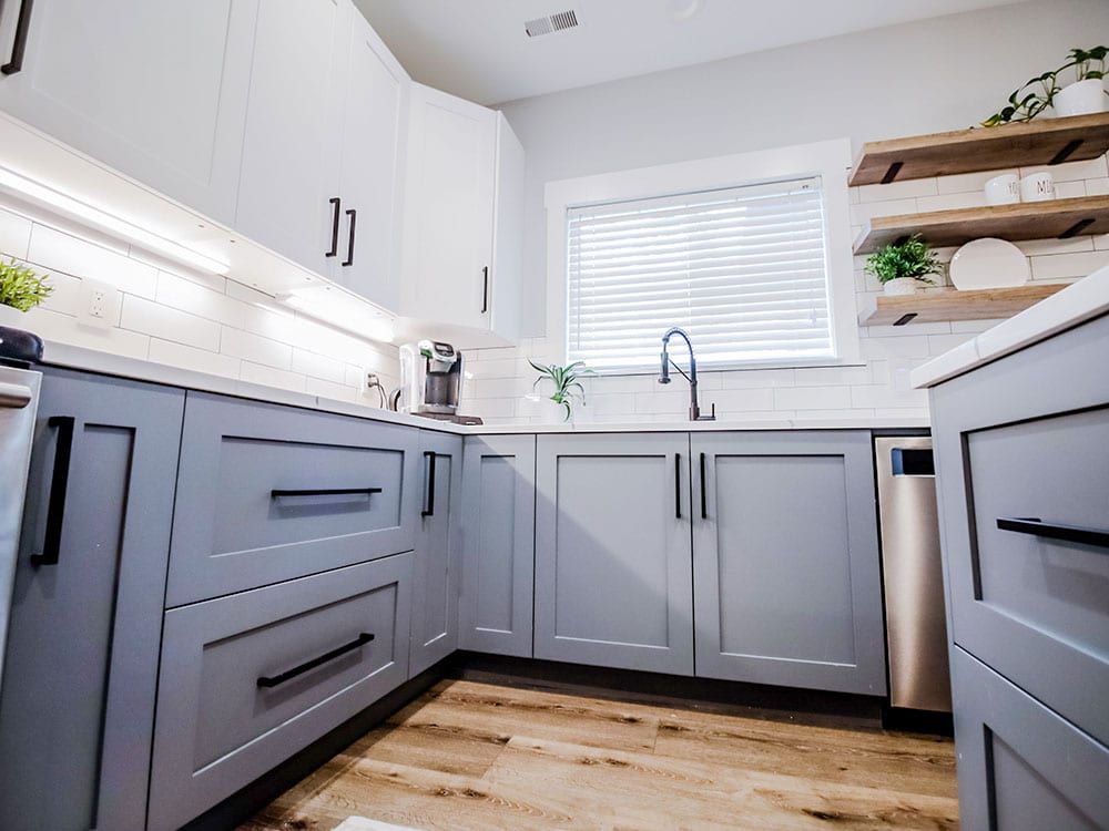 A kitchen with gray cabinets , stainless steel appliances , a sink , and a window.