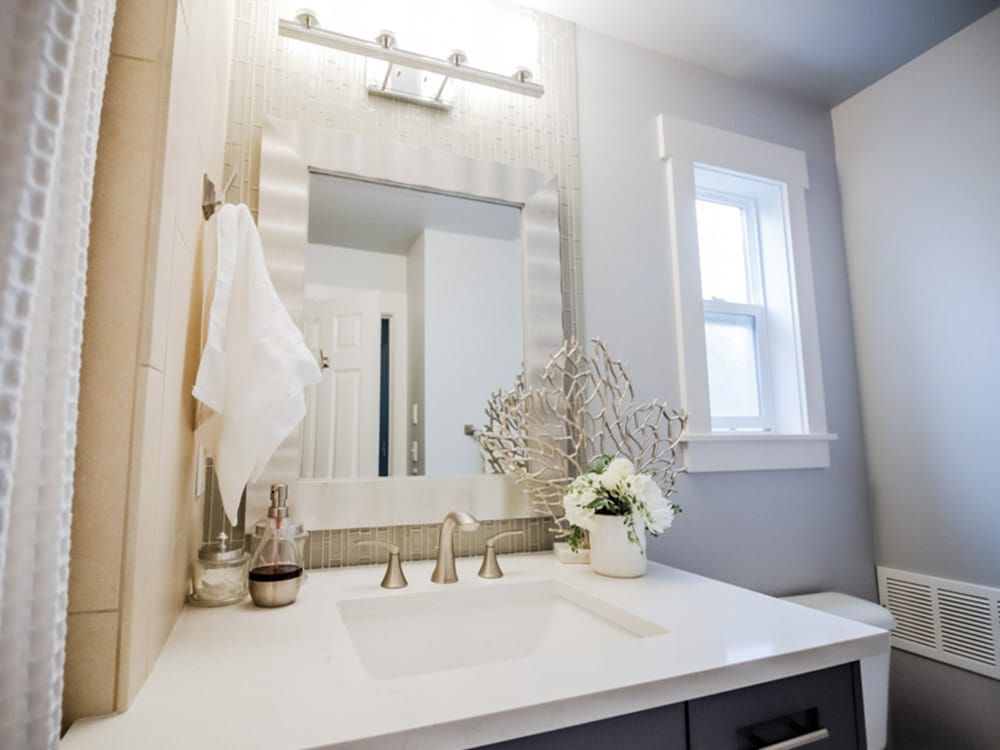 A bathroom with a sink , mirror and window.
