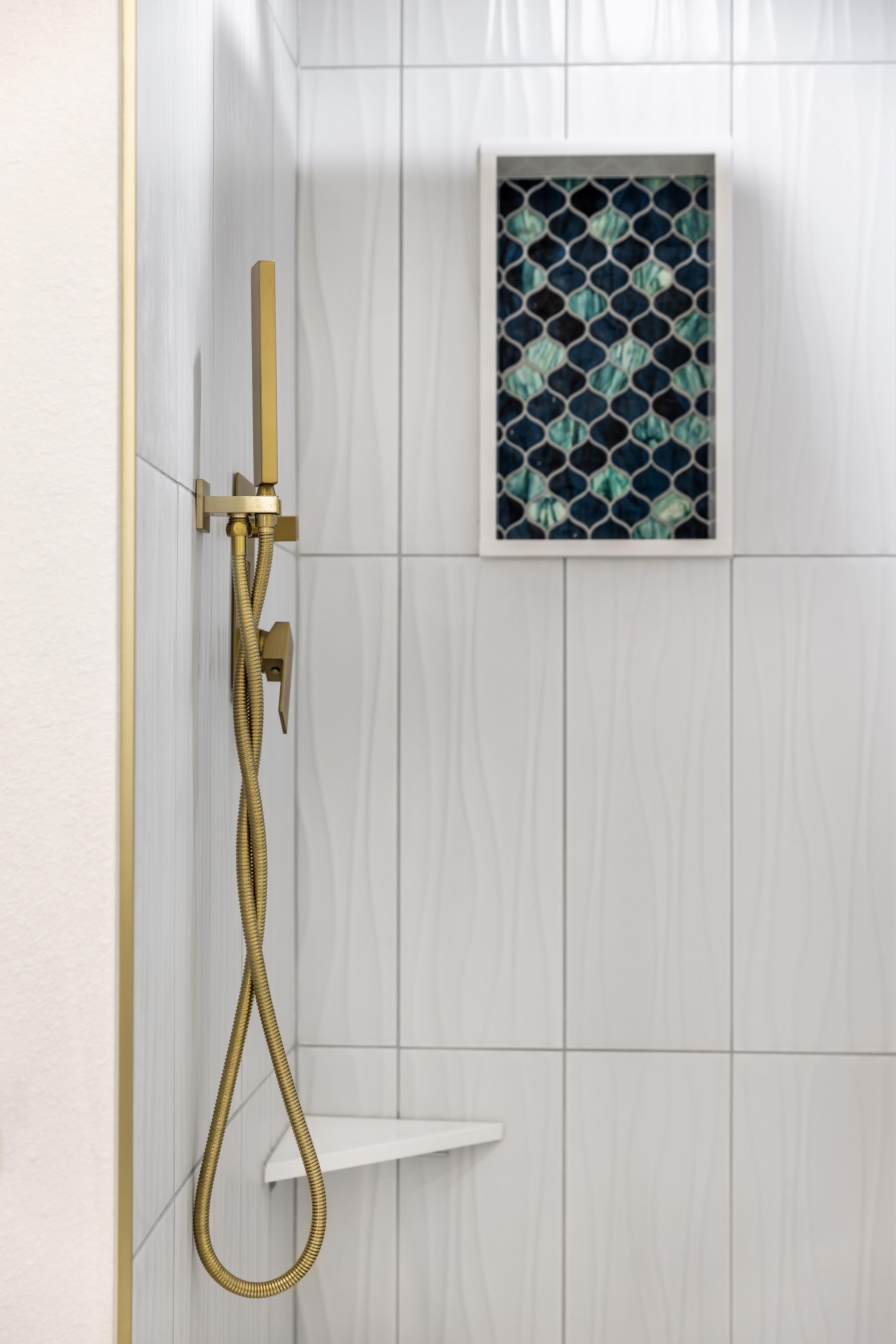 A shower with a brass shower head and a shelf.