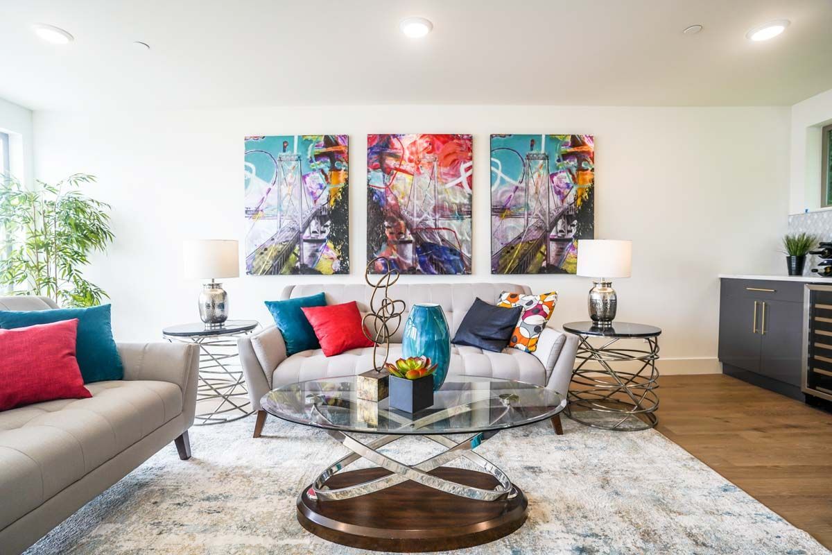 A living room with a couch , chair , coffee table and paintings on the wall.