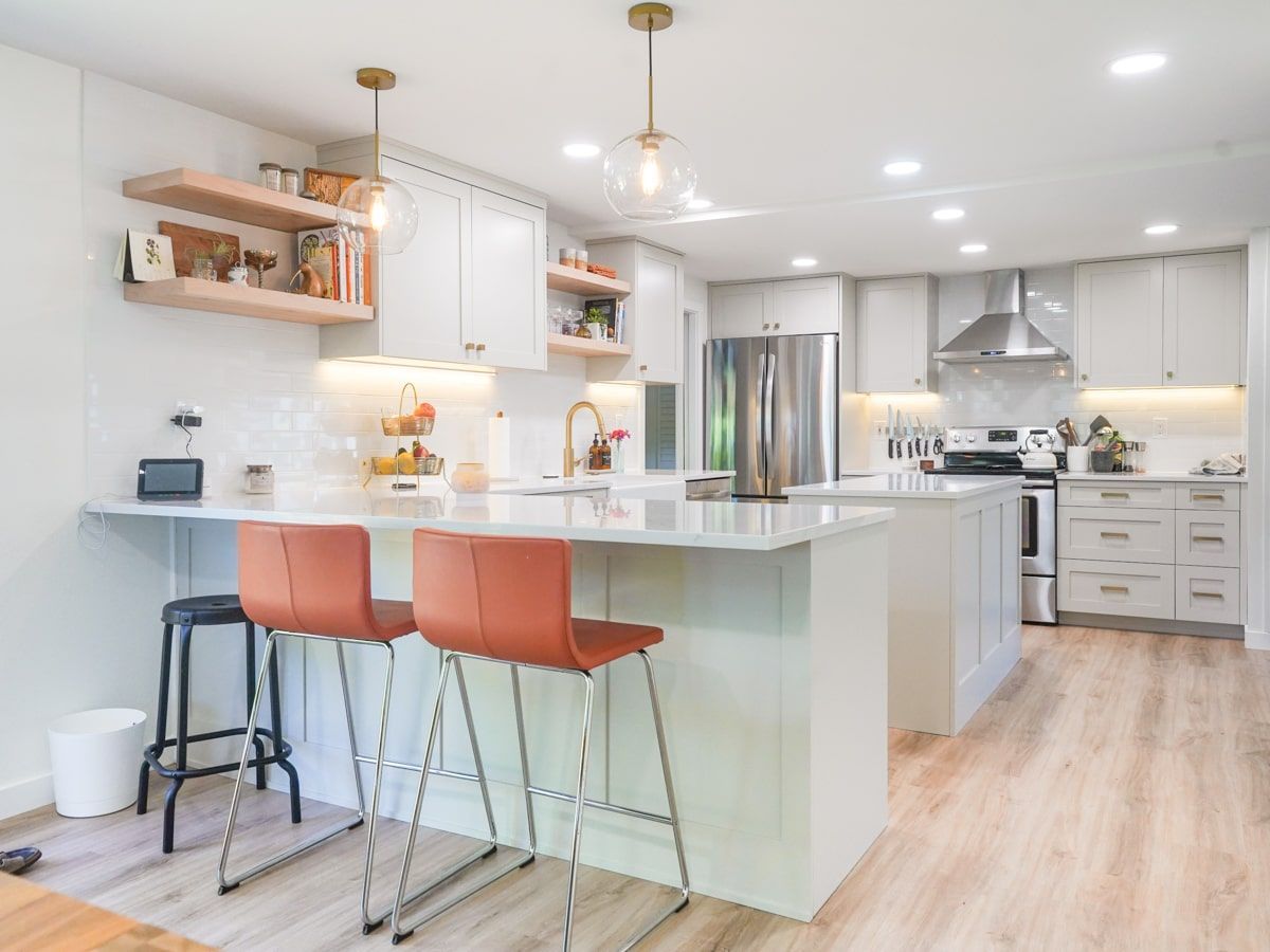 A kitchen with white cabinets , stainless steel appliances , a large island , and two bar stools.
