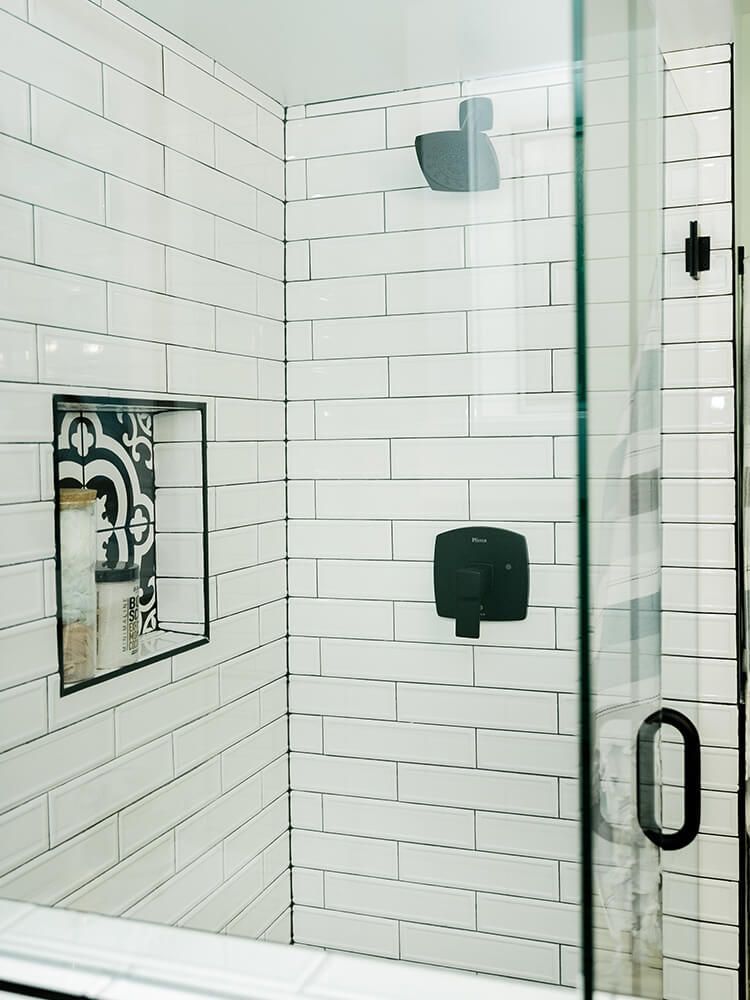 A bathroom with white subway tiles and a walk in shower with a glass door.