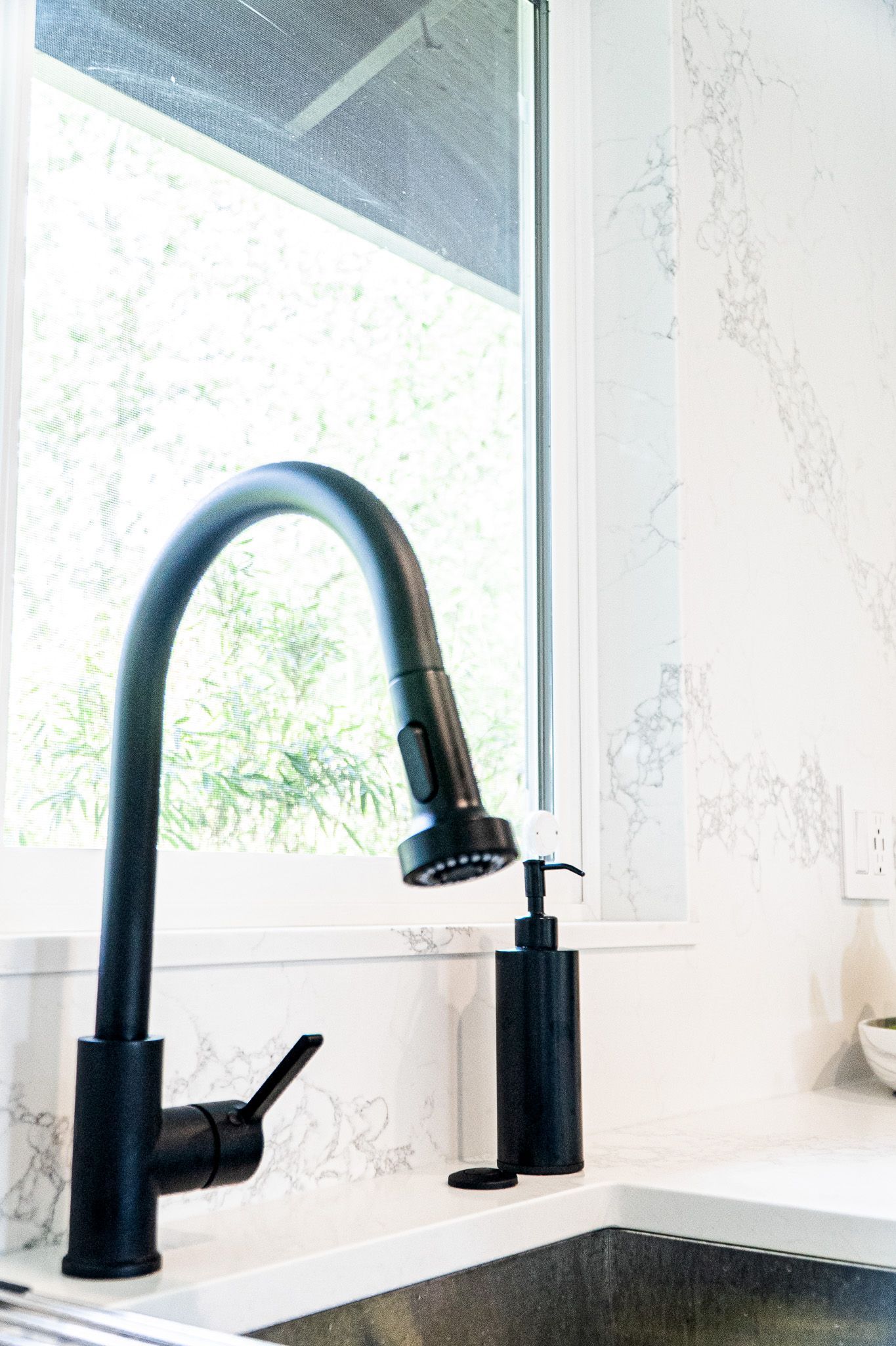 A kitchen sink with a black faucet and soap dispenser next to a window.
