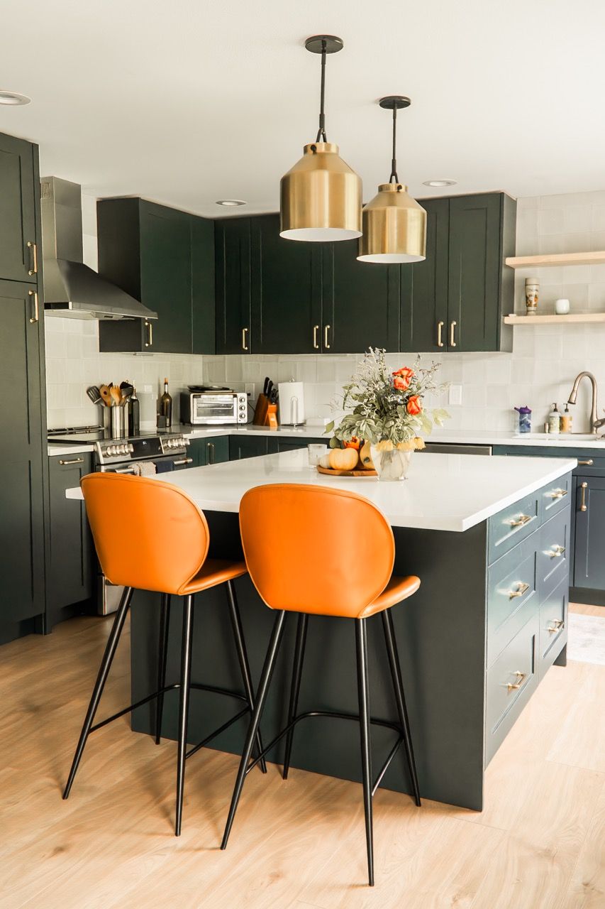 A kitchen with a large island and two orange bar stools.