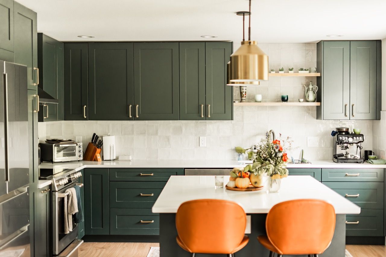 A kitchen with green cabinets and orange chairs and a large island.