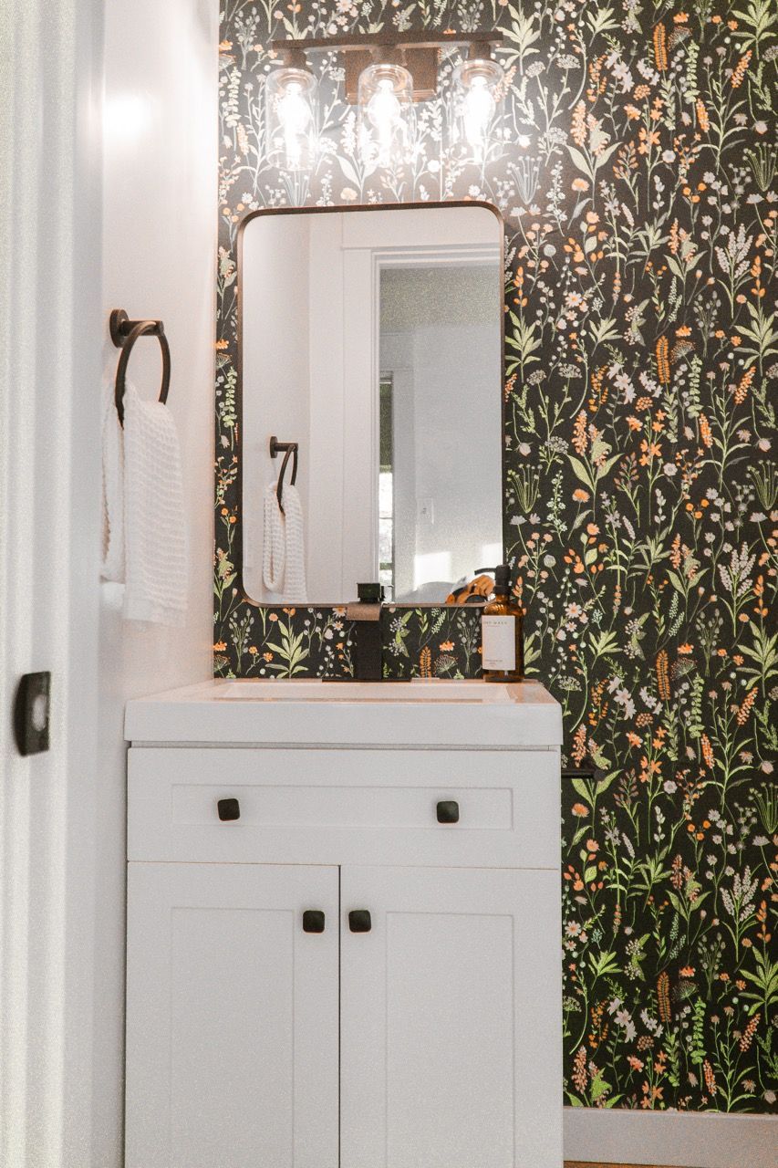 A bathroom with a sink , mirror , and floral wallpaper.