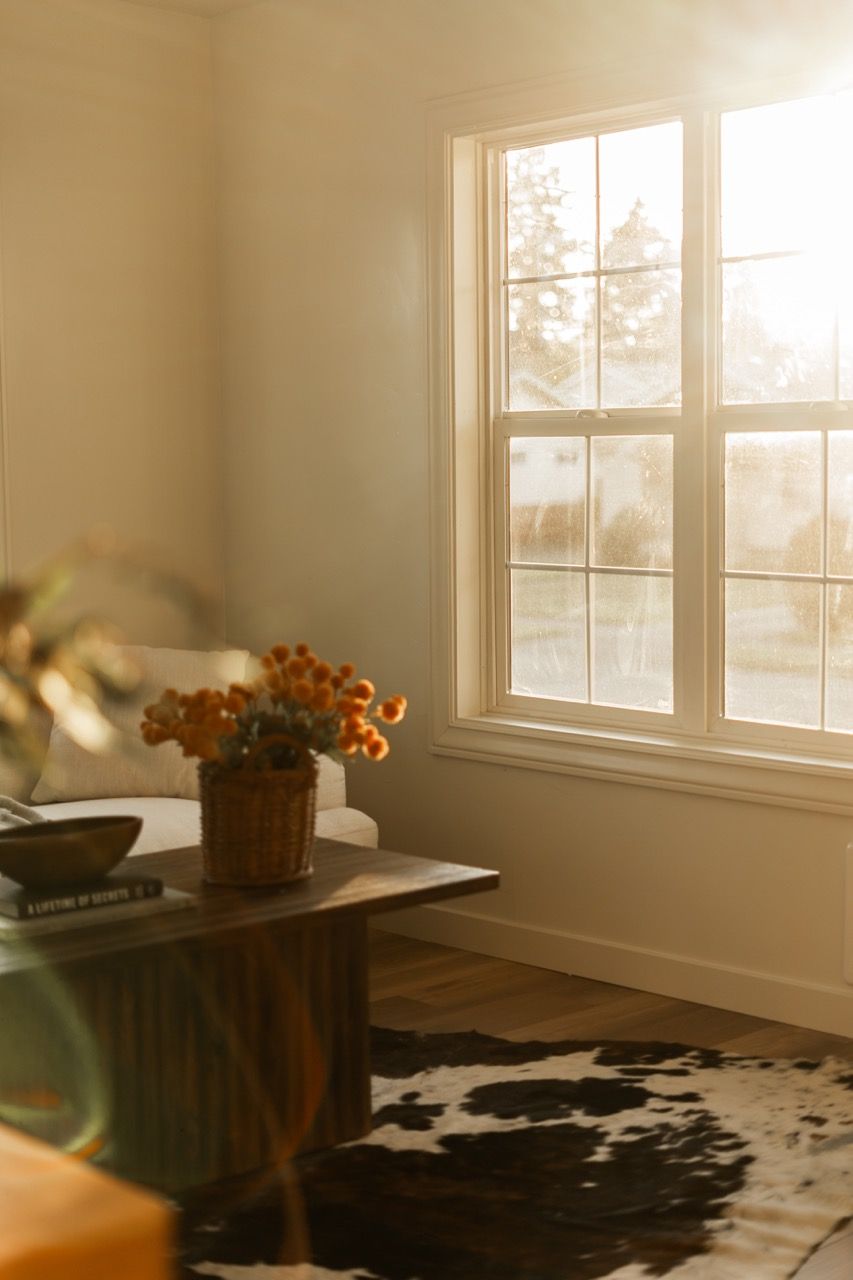 A living room with a cow print rug , a coffee table , and a window.