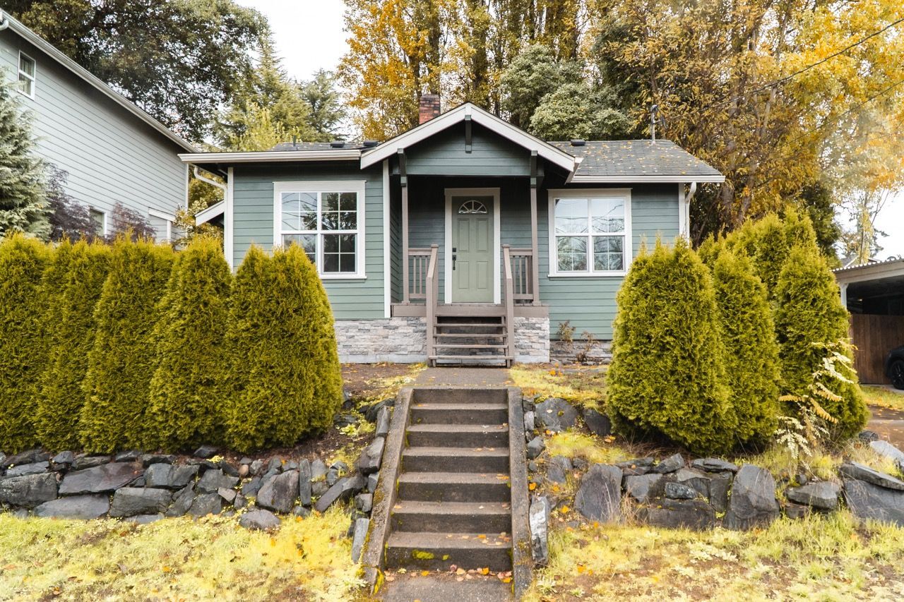 A small house with stairs leading up to it is surrounded by trees and bushes.