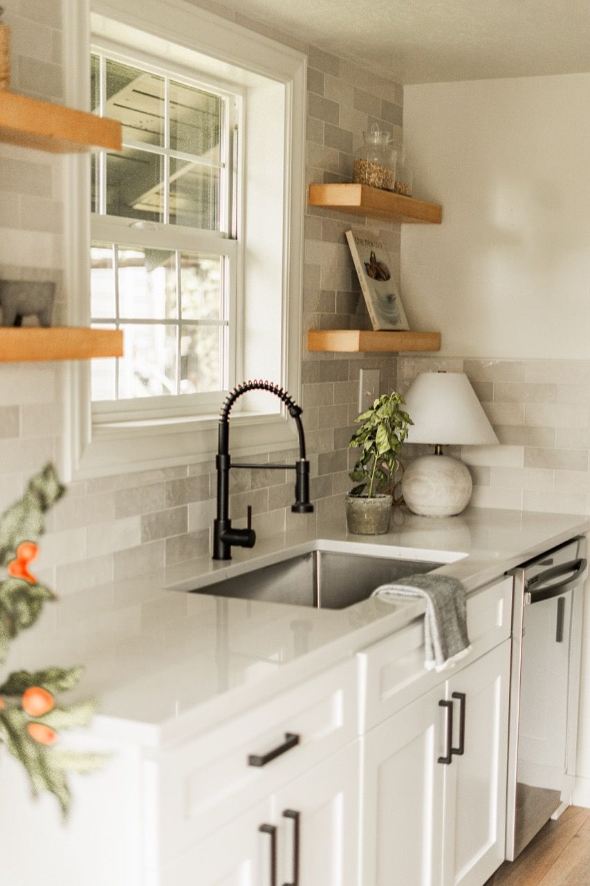 A kitchen with white cabinets , a sink , and a window.