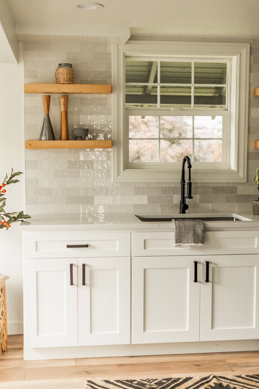 A kitchen with white cabinets , a sink , and a window.