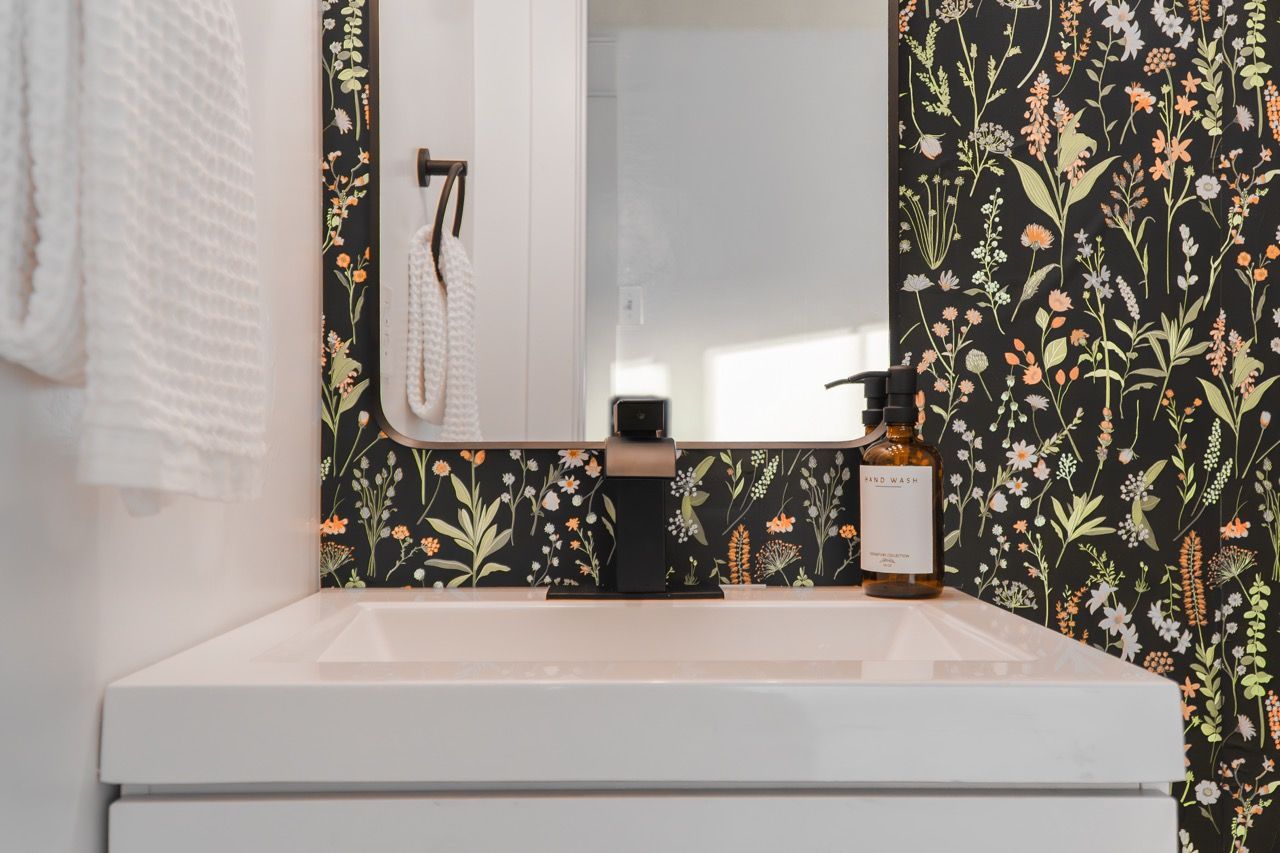 A bathroom with a sink , mirror and floral wallpaper.