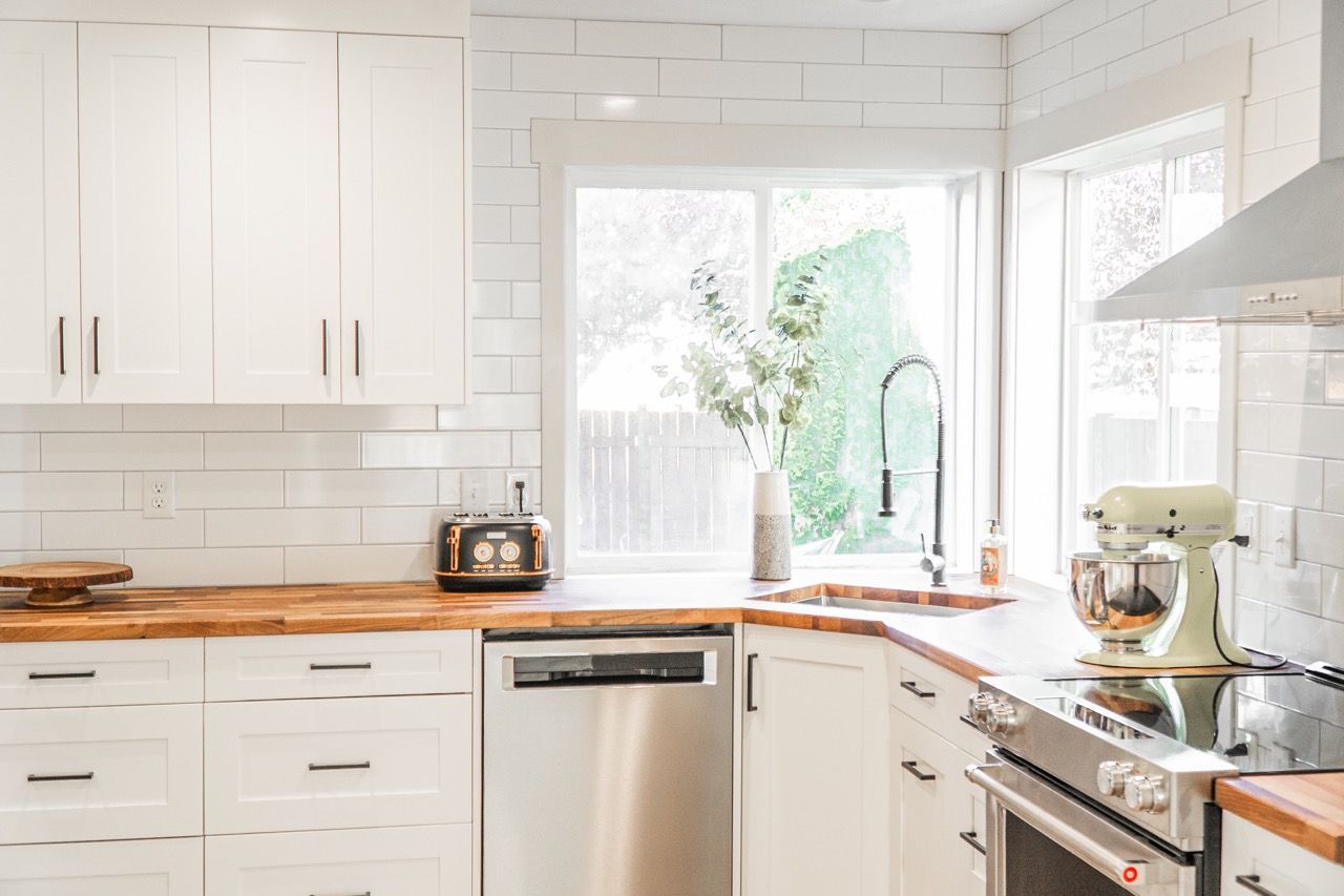 A kitchen with white cabinets , stainless steel appliances , wooden counter tops and a window.
