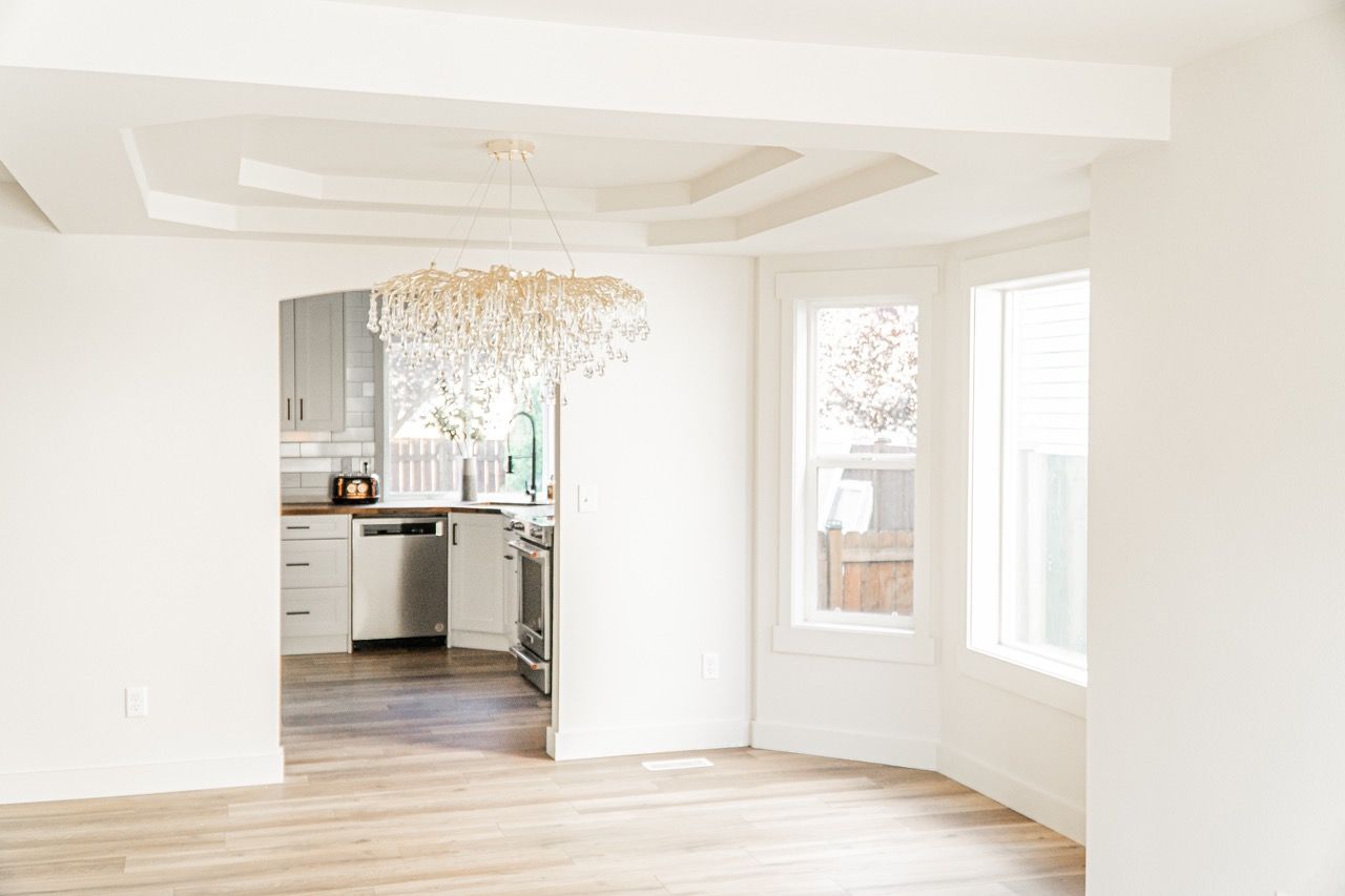 An empty room with a kitchen in the background and a chandelier hanging from the ceiling.