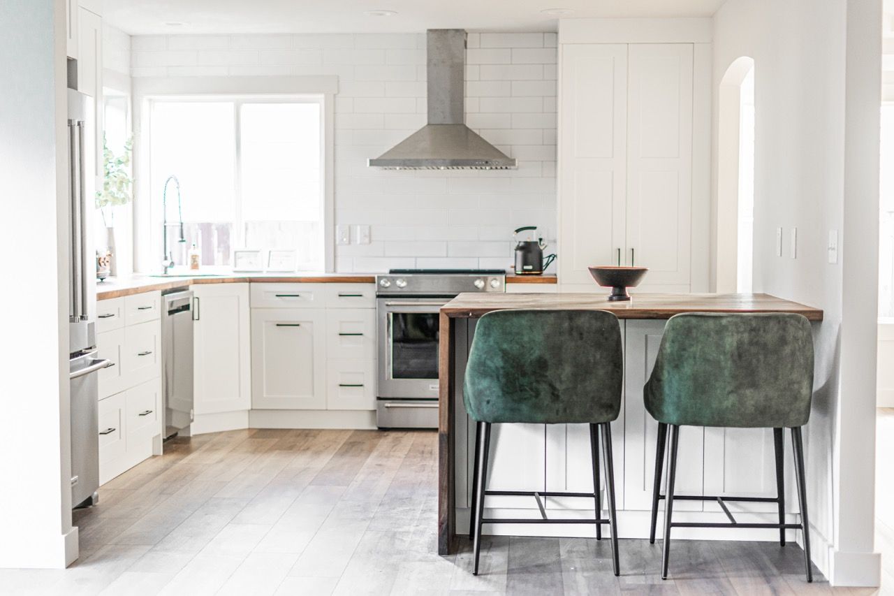 A kitchen with white cabinets , stainless steel appliances , and green bar stools.