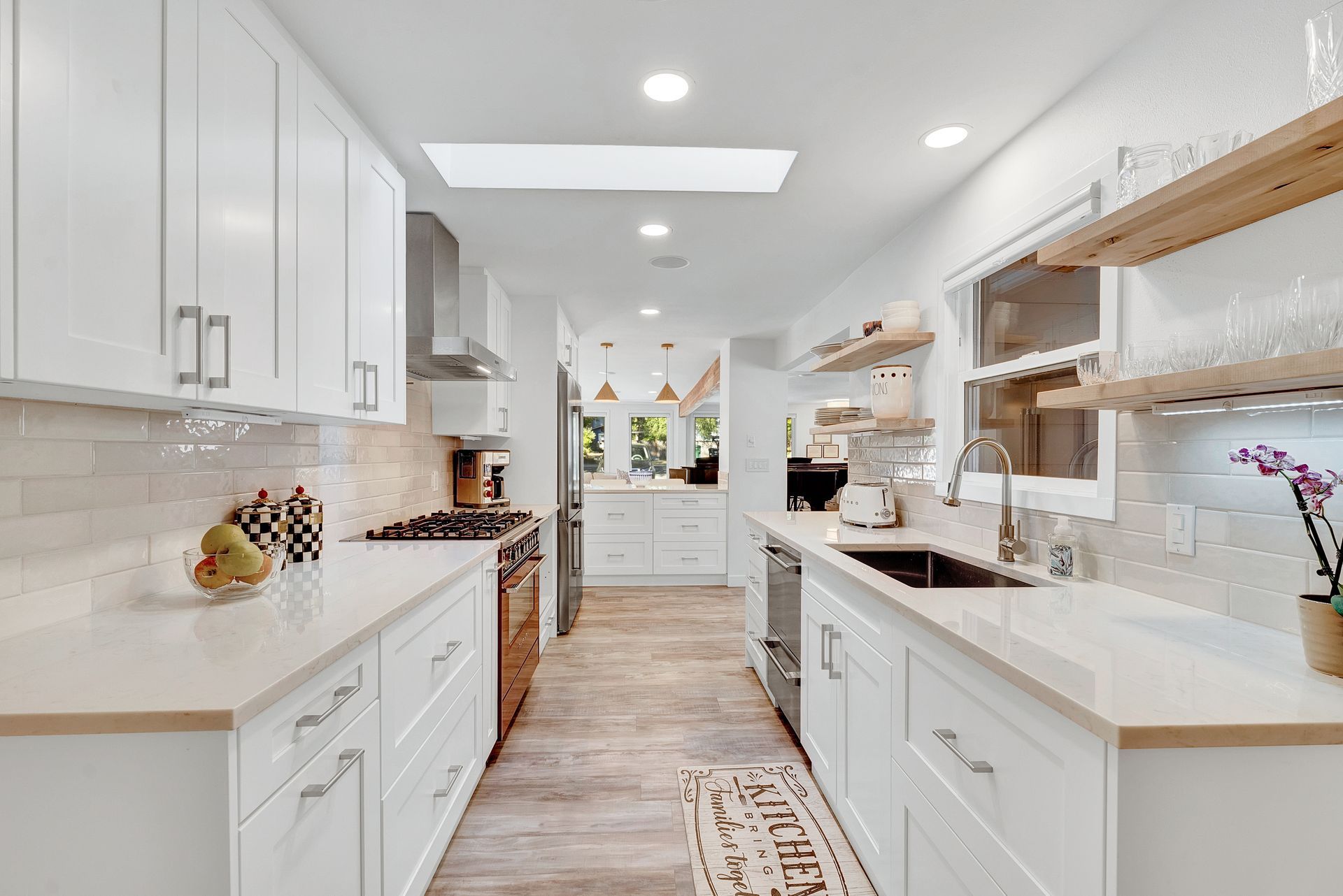 A kitchen with white cabinets , stainless steel appliances , a sink , and a skylight.