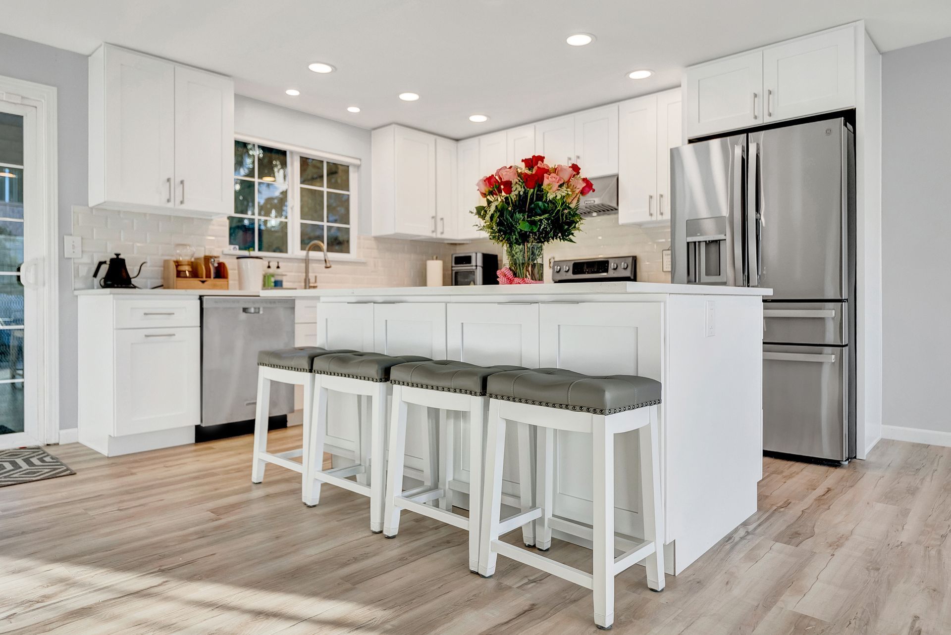 A kitchen with white cabinets , stainless steel appliances , and a large island with stools.