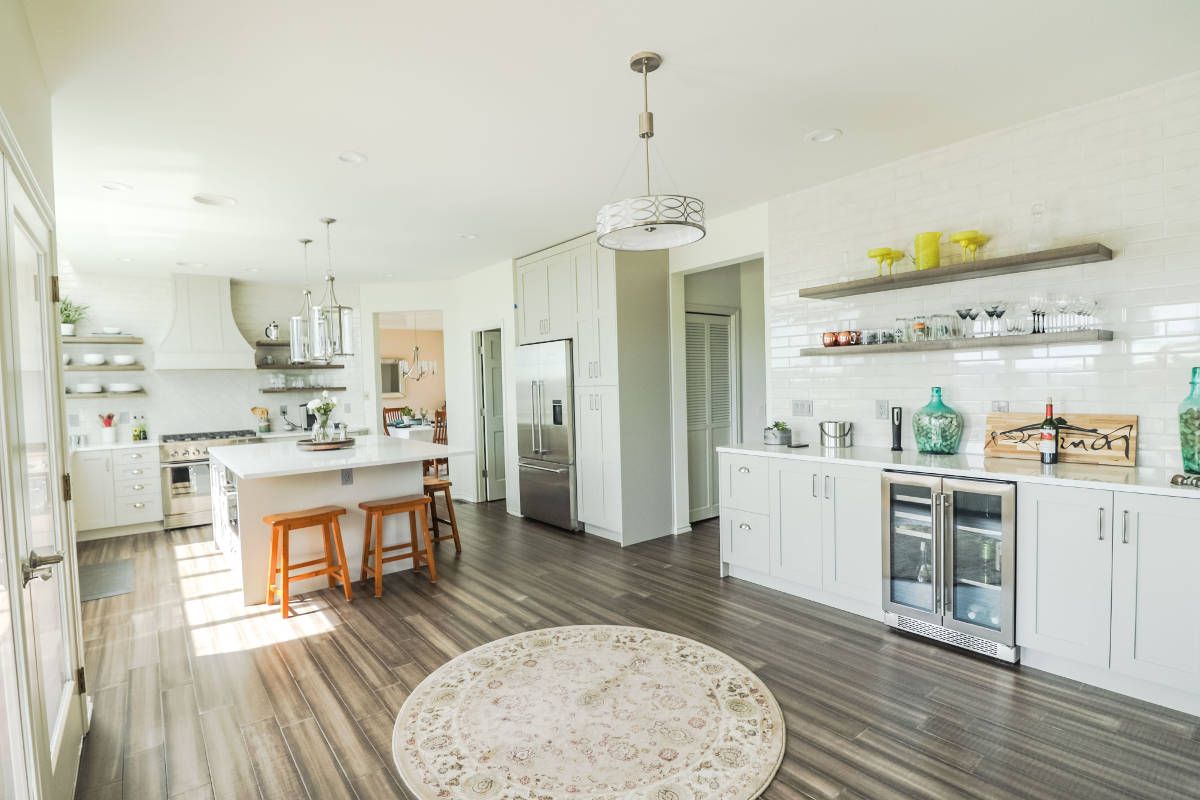 A kitchen with white cabinets , wooden floors , stools and a rug.
