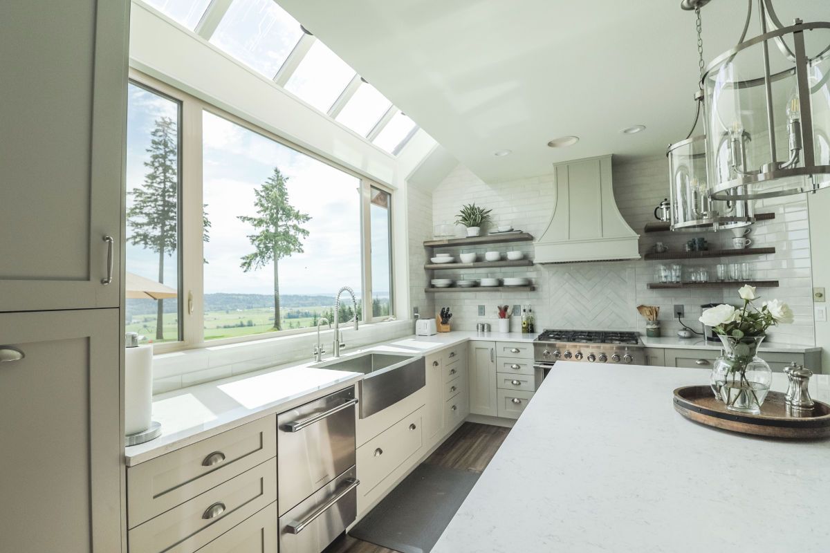 A kitchen with white cabinets and stainless steel appliances and a large window.