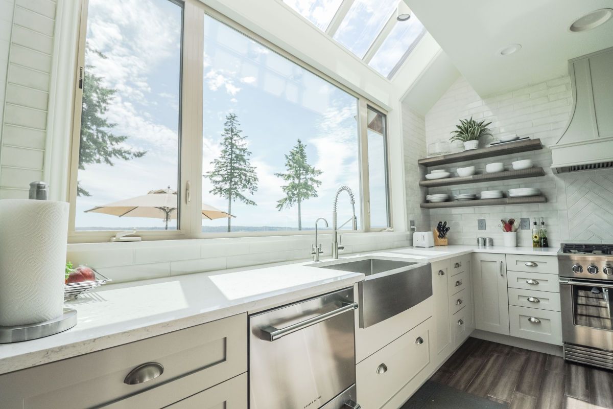 A kitchen with white cabinets , stainless steel appliances , a sink and a large window.