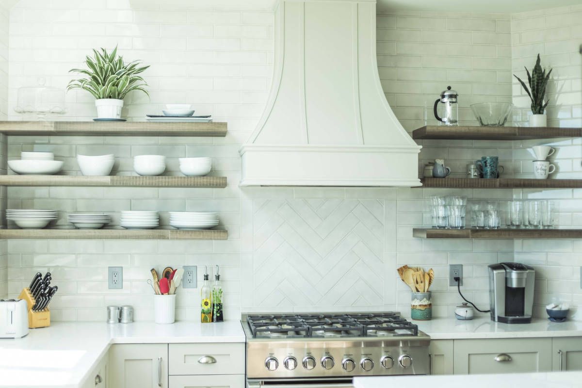 A kitchen with a stove , sink , and shelves.