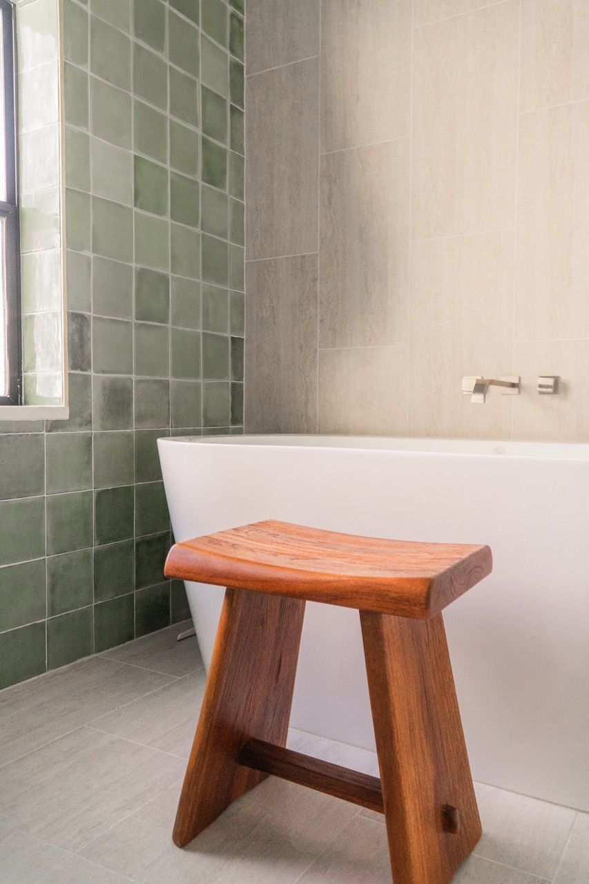 A wooden stool is sitting next to a bathtub in a bathroom.