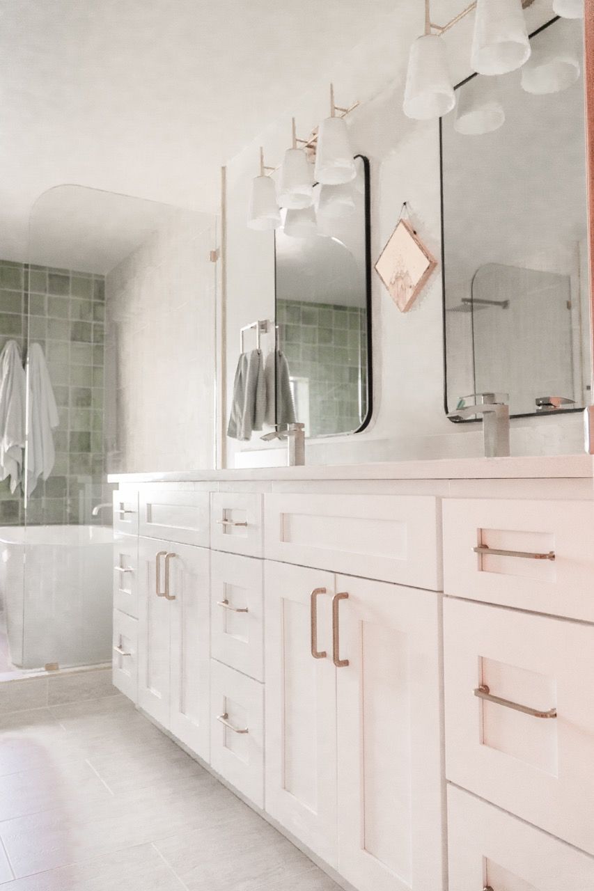 A bathroom with white cabinets , drawers , a sink and a mirror.