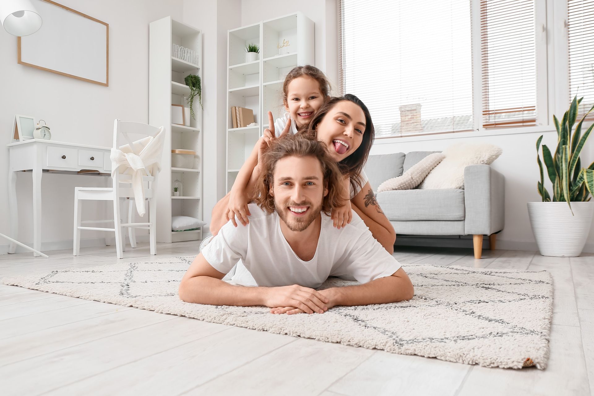 A man is laying on the floor with his wife and daughter on his shoulders.