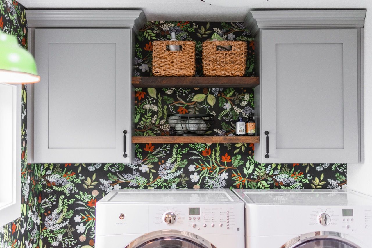 A laundry room with a washer and dryer and a floral wallpaper.