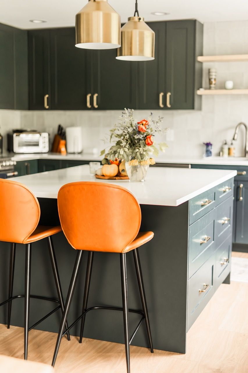 A kitchen with a large island and two orange bar stools.