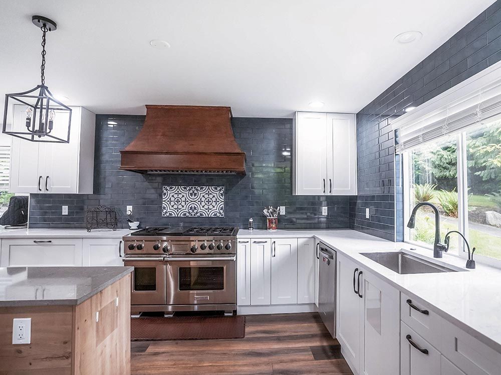 A kitchen with white cabinets , a stove , a sink , and a large window.