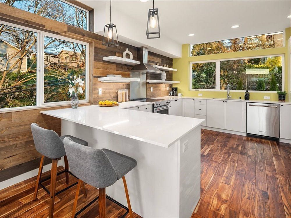 A kitchen with hardwood floors , white cabinets , stainless steel appliances and a large island.