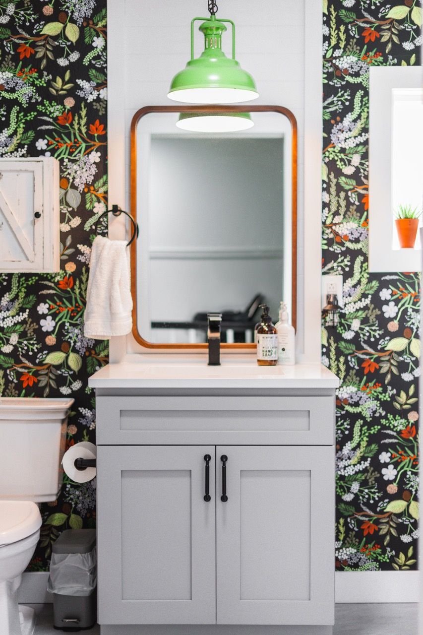 A bathroom with a sink , toilet , mirror and floral wallpaper.