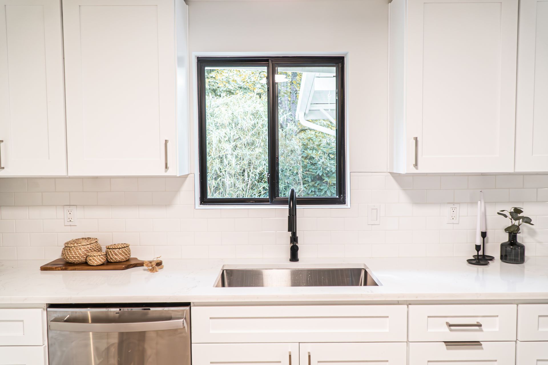 A kitchen with white cabinets , stainless steel appliances , a sink and a window.