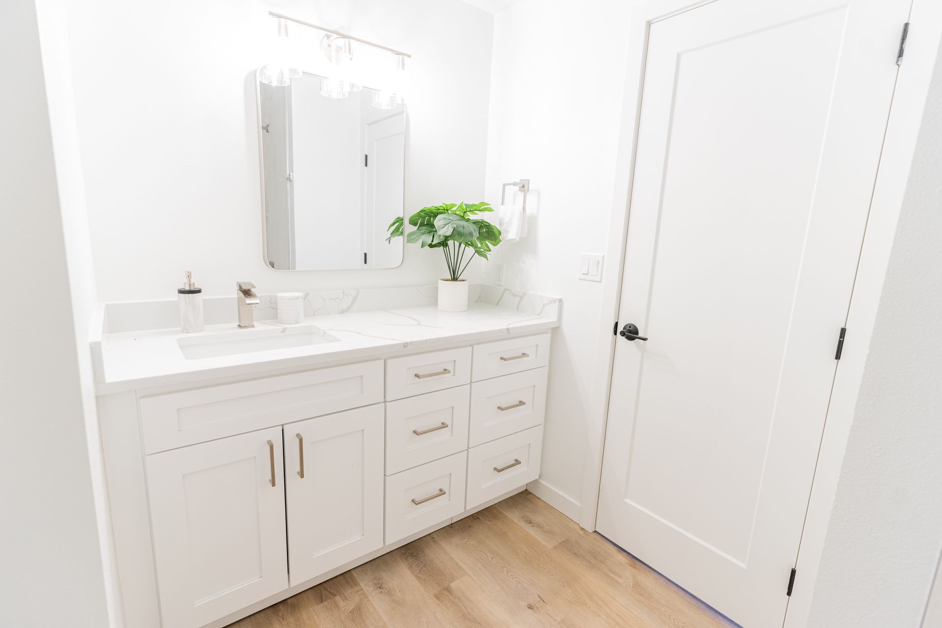 A bathroom with white cabinets , drawers , a sink and a mirror.