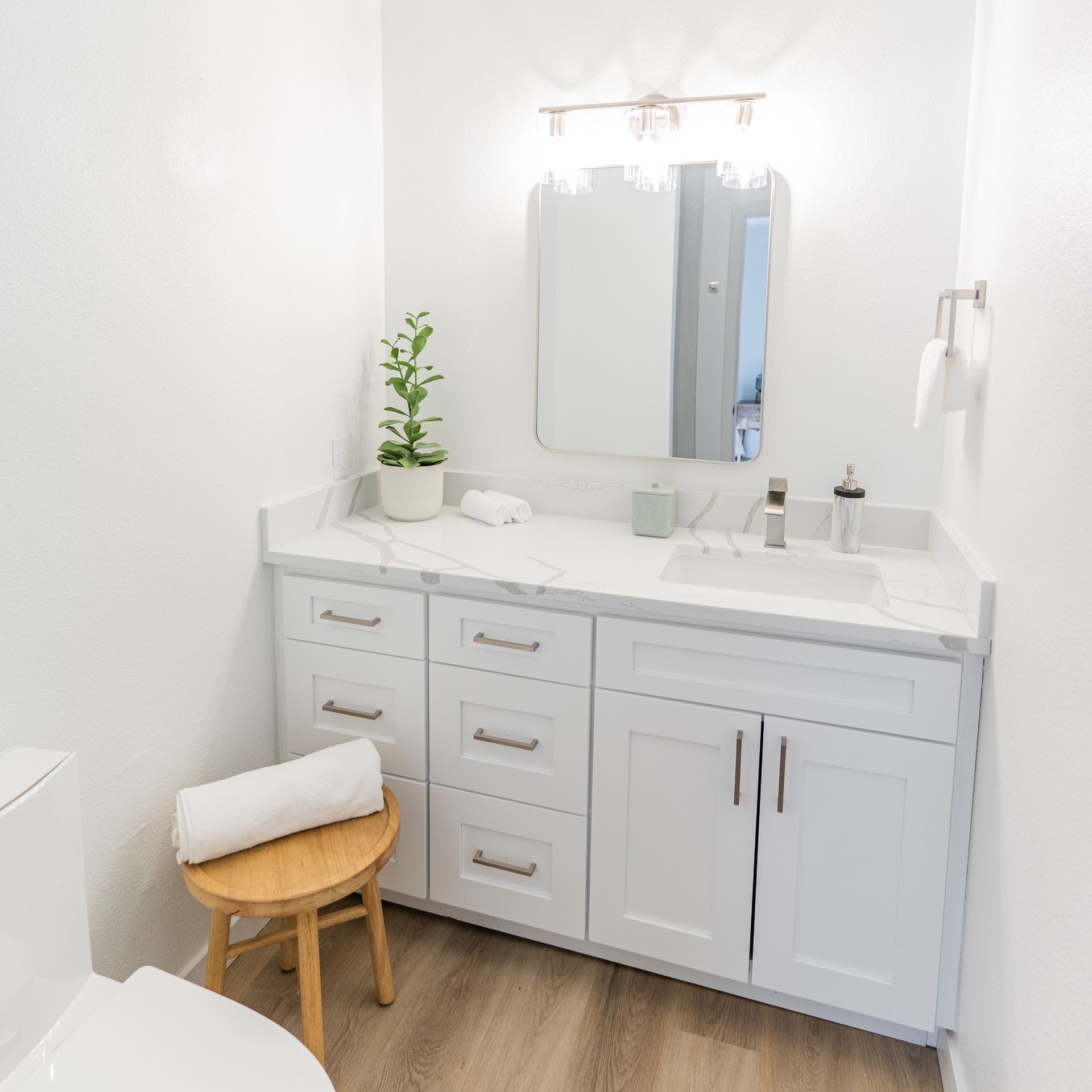 A bathroom with white cabinets , a toilet , a sink and a mirror.