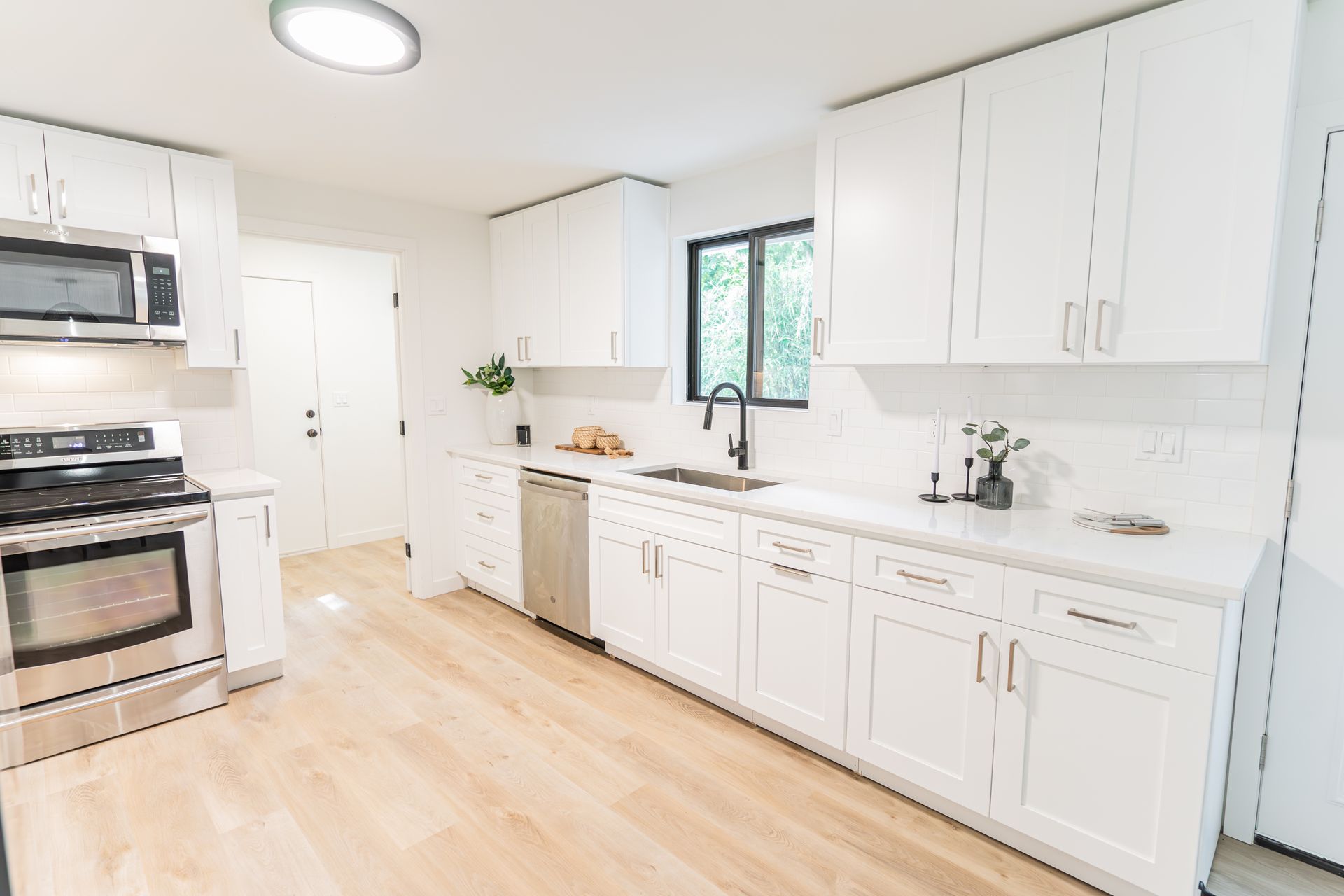 A kitchen with white cabinets , stainless steel appliances , a sink , and a window.